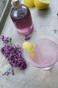 a glass filled with purple liquid next to two lemons and some lavender sprigs