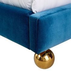 a blue couch with white pillows and a gold ball on the bottom of it's headboard