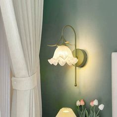 a lamp that is on the side of a wall next to a table with flowers