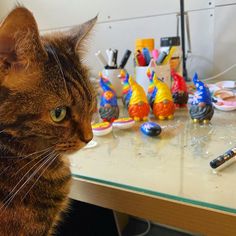 a cat sitting on top of a table next to toy figurines and pens