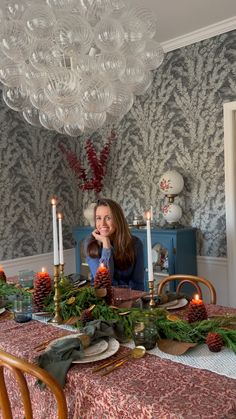 a woman sitting at a table with candles in front of her and christmas decorations on the table