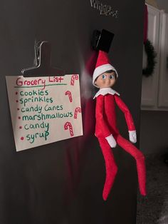 an elf hanging from the side of a refrigerator next to a sign that says grocery list