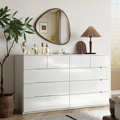 a white dresser sitting next to a mirror and a potted plant in a living room