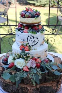 a three tiered cake with berries and greenery on top sits on a table outdoors