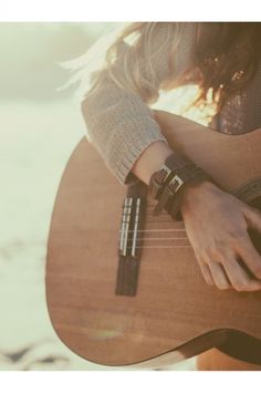 a close up of a person holding a guitar on the beach with sand in the background