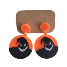 an orange and black pair of earrings with a skull on the front, and a pumpkin behind it