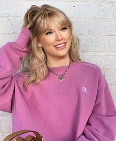 a woman with blonde hair wearing a pink sweater and holding a brown purse in her hand