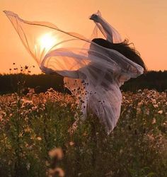 a woman in a field at sunset with her veil flying