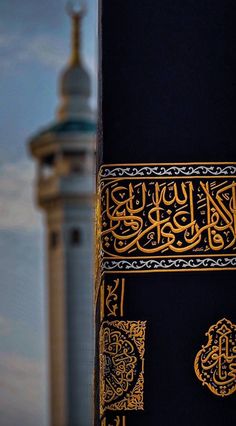 an arabic calligraphy on the side of a tall building with a clock tower in the background