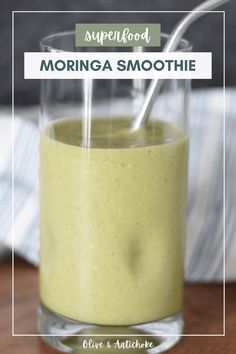 a glass filled with green smoothie sitting on top of a wooden table