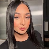 a woman with long black hair standing in front of a stove top oven and looking at the camera