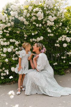 mother and daughter sitting on the ground in front of white flowers with their mouths open