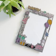 a happy birthday photo frame next to a potted plant on a white table top