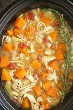 a crock pot filled with chicken, carrots and potato soup next to a sprig of rosemary