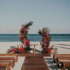 two wooden benches sitting on top of a beach next to the ocean with flowers growing out of them