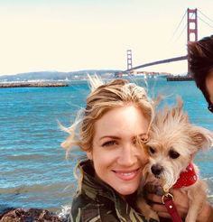 a woman holding a dog in front of the golden gate bridge