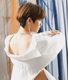 a woman with short hair wearing a white shirt and silver hoop earrings, standing in front of a curtain