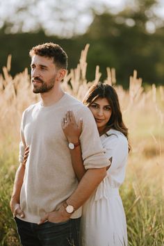 a man and woman are standing in tall grass with their arms around each other as they look at the camera