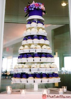 a large multi tiered cake sitting on top of a white table covered in cupcakes