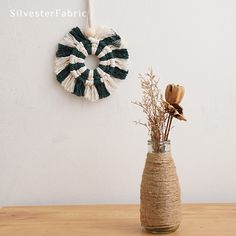 a vase with some flowers in it next to a wall hanging on the wall and a rope