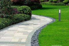 a walkway in the middle of a lush green park with shrubs and flowers on either side