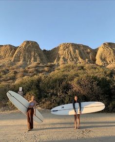 two women with surfboards standing in the sand