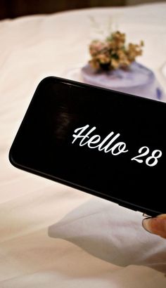 a person holding up a cell phone with the words hello 28 written in white on it