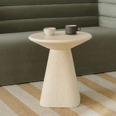 a white table with two cups on it sitting in front of a gray couch and striped rug