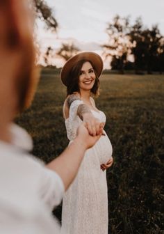 a pregnant woman in a white dress and hat holding the hand of a man wearing a brown hat