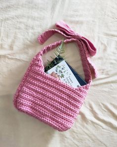 a pink crocheted purse with a book in it on a white bed sheet