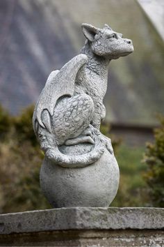 a statue of a dragon sitting on top of a stone ball in front of some bushes