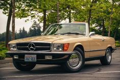 a tan mercedes benz is parked in a parking lot with trees and bushes behind it