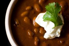 a close up of a bowl of beans with sour cream and cilantro on top