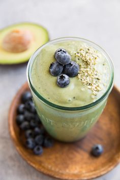 an avocado smoothie with blueberries and oats on a wooden plate