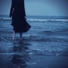 a woman standing in the ocean with an umbrella