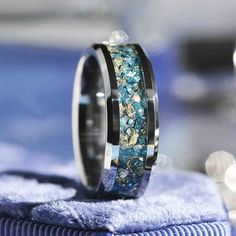 a wedding ring with blue and green stones on it sitting on top of a towel