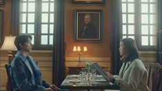 a man and woman sitting at a table in a dining room with paintings on the walls