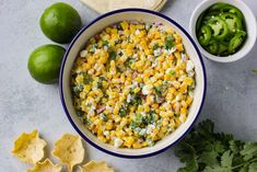 a bowl filled with corn, cilantro and cheese next to tortilla chips