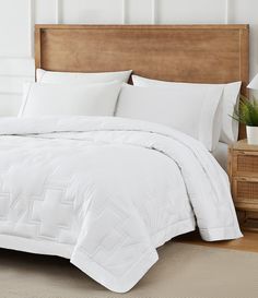 a bed with white comforter and pillows on it in a small room next to a wooden headboard