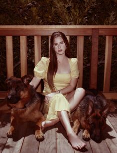 a woman in a yellow dress sitting on a wooden deck with two dogs next to her