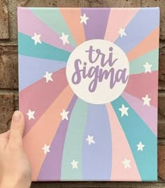 someone holding up a canvas with the word tri stigma on it in front of a brick wall