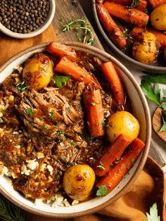 two bowls filled with meat, potatoes and carrots next to other food on a wooden table