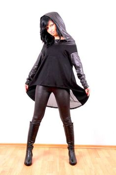 An eye-catching global inspired design, this hooded black tunic dress is an easy-to-wear modern top which will give you a flattering silhouette. Crafted from a black jersey knit with leather sleeves and hood, this tunic dress is not only comfortable but has an edgy style that will set you aside. Try something new today! The tunic can be worn with leggings or skinny jeans and boots. For colder weather, it can be worn over a long sleeve top or on its own for nights out. Available in sizes from XS to XL, this is a top for any shape. The asymmetrical hemline is wonderfully flattering. XS (2-4) Bust approx. 33,5" / 85 cm Waist              26"  / 66 cm Hip                 36"  / 91 cm S (6-8) Bust               35,5" / 90 cm Waist             28"    / 71 cm Hip                 38"   /  97 cm M Edgy Stretch Hoodie For Fall, Black Hoodie For Fall Layering, Black Hooded Hoodie For Layering, Black Tunic Dress, Edgy Streetwear, Modern Tops, Streetwear Mode, Tunic Hoodie, Leather Sleeves