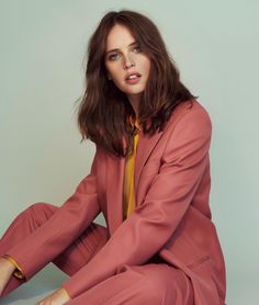 a woman sitting on the ground wearing a pink suit and yellow tie with her legs crossed