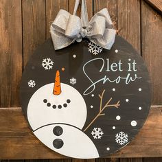 a wooden sign that says let it snow with a snowman wearing a santa hat