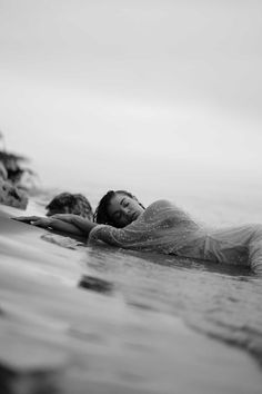 a woman laying on top of a surfboard in the ocean next to another person