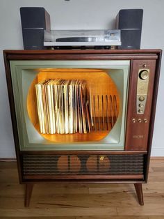 an old fashioned television set with many books on the front and side, sitting on top of a wooden floor