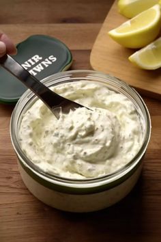 a person holding a spoon over a jar of mayonnaise with lemons on the side