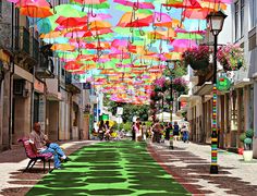 people sitting on benches under colorful umbrellas in an alleyway with buildings and street lights