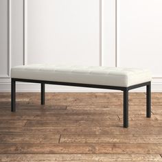 a bench sitting on top of a wooden floor next to a white wall in a room